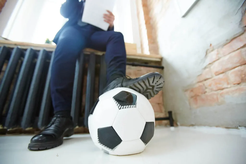 Ein Mann mit Ball am Fuß sitzt auf einer Heizung