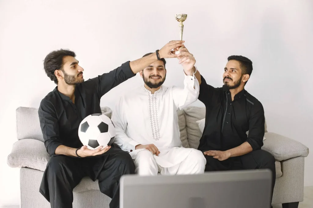 Fans schauen Fußball vor dem TV und halten einen Pokal hoch