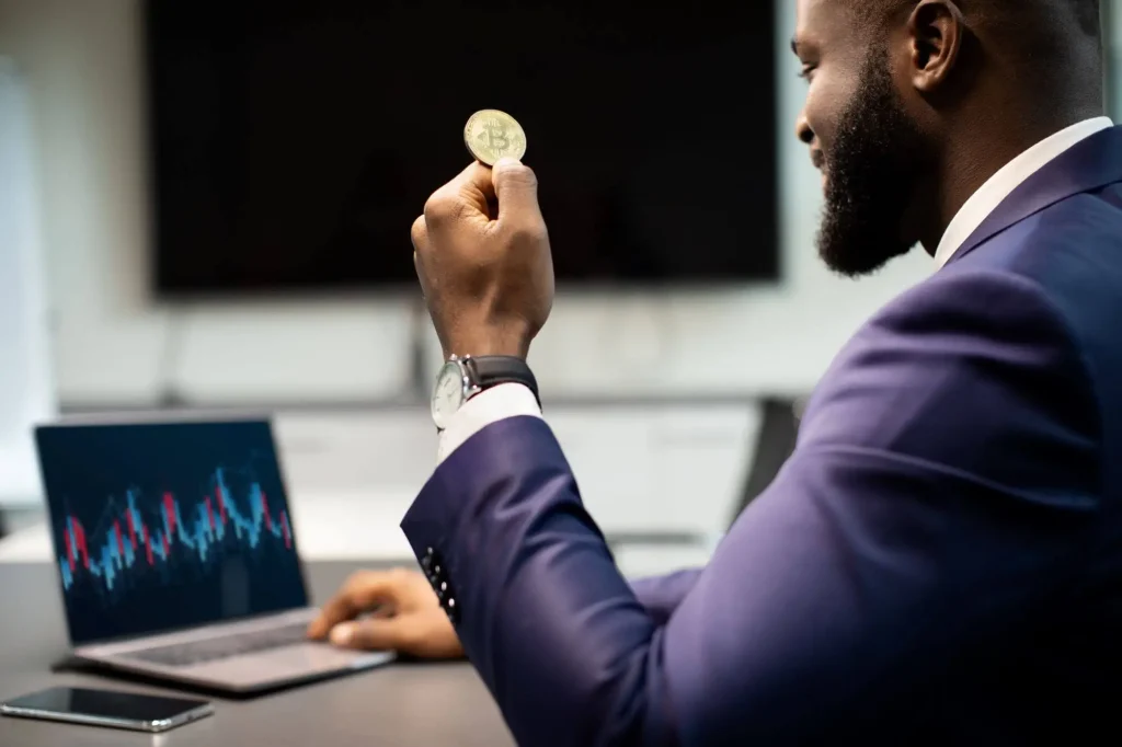 Ein Mann sitzt am Laptop mit Bitcoin-Münze